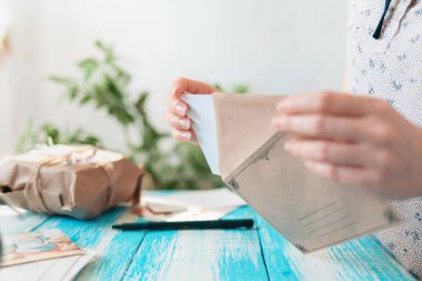 Bir kadın el işi zarfına kartpostal koyar. Eller yakın çekim. Posta iletisi kavramı.