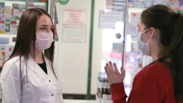 药剂师和顾客在药店里交流 戴口罩的女人从买方的肩上看过去 病毒大流行病的概念和防止感染 — 图库视频影像