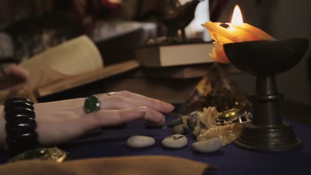 占星术和神秘主义 一位妇女算命师翻阅一本书 用手指敲敲桌子 旁边点着一支燃着的蜡烛滴着蜡 手拿着戒指和手镯 侧视图 — 图库视频影像
