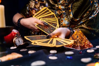 Astroloji ve ezoterizm. Bir falcının elinde Tarot kartları hayranı var. Masanın üzerinde rünler ve tılsımlar var. Ellerin yakın çekimi.