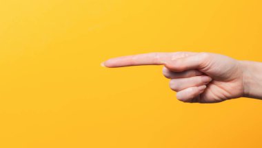 Kadın eli yakın plan, uzun işaret parmağı bir şeyi işaret ediyor. Yön bulma hareketi. Sarı arka plan. Boşluğu kopyala.