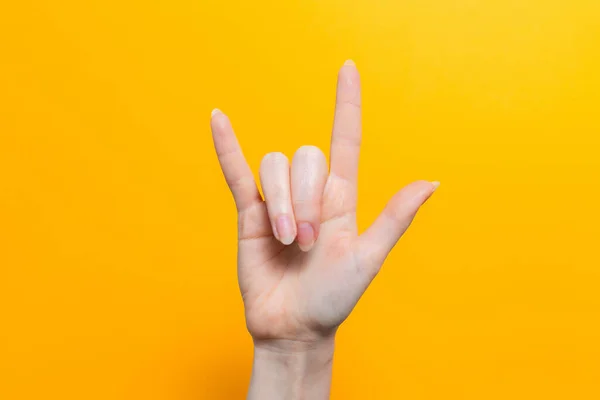Female hand in the gesture of a goat close-up on a yellow background. Copy space.