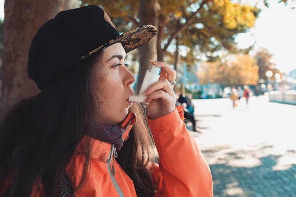 Chronic disease. Portrait of a teenage girl using an inhaler on the street, having an asthma attack. Side view. Outdoor.