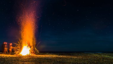 Bir adamın silueti enkazdan plajı temizler, dalları yakar, ışık saçar..