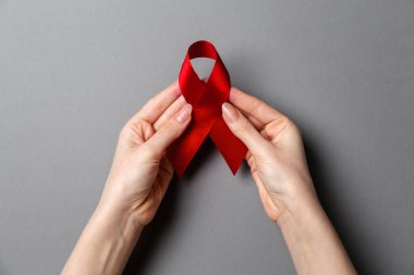 Kadının ellerinde AIDS 'le mücadelenin sembolü olan kırmızı bir kurdele var. Gri arka plan. Uzayı kopyala Düz yatıyordu. Dünya AIDS Günü konsepti.