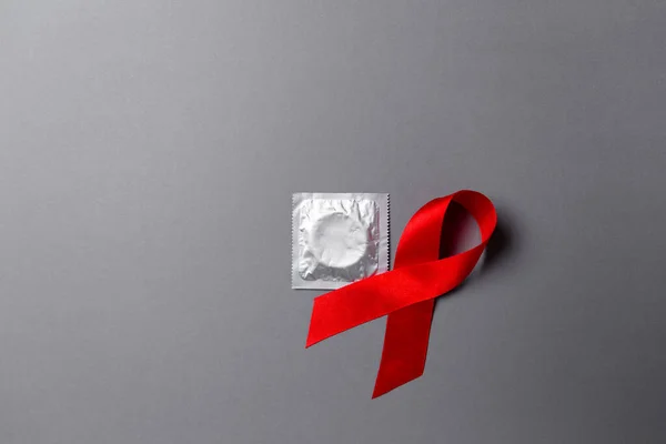 The concept of world AIDS day and safe sex. Red ribbon and condom on a gray background. Copy space. Flat lay.