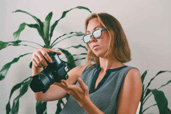 創造的でオフィスの仕事 カメラを覗き込む眼鏡をかけた若い女性写真家 背景には 植物の葉 — ストック写真