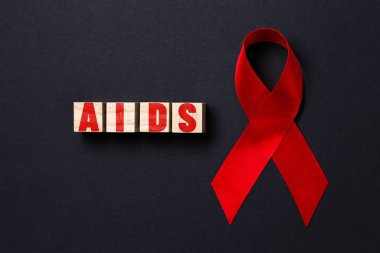 Siyah arka planda AIDS yazan kırmızı kurdele ve tahta küplerle. Kapatın. Düz yatıyordu. Dünya AIDS Günü konsepti.