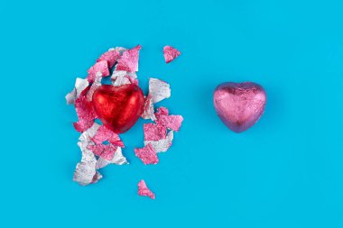 14 Şubat ya da Sevgililer Günü kavramı. Kırmızı ambalajlı bir kalp çikolatası ve şekerden koparılmış bir paket ve pembe bonbon. Açık mavi arka plan. Boşluğu kopyala.