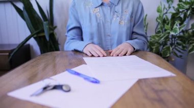 Bir kadın anahtarları alır ve belgeleri masaya doğru iter. Kağıtları ve elleri yakın çekim masası. Kiralama kavramı.