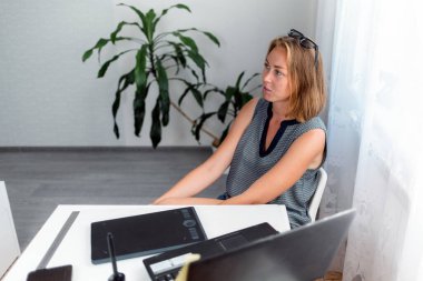 Serbest çalışıyorum. Genç bir kadın iş hakkında düşünmeye devam ediyor. Masanın üzerinde bir dizüstü bilgisayar ve tablet var. Üst Manzara. Kendini izole etme, karantina ve uzak çalışma kavramı..