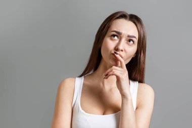 Fikir ve bilgi araması kavramı. Suratı asık genç, düşünceli, beyaz bir kadının portresi. Gri arka plan. Boşluğu kopyala.