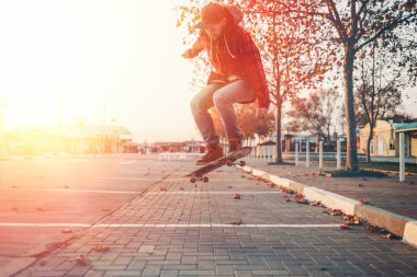 Kaykay yapmak. Adam kaykayla Ollie dublörlüğü yapıyor. Havaya zıpla. Arka planda sokak var. Güneş ışığı.