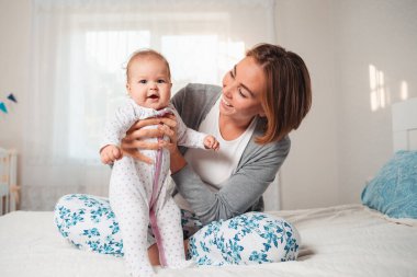 Yatakta otururken elinde gülümseyen bir bebek tutan mutlu bir anne. Annelik ve çocuk bakımı kavramı.
