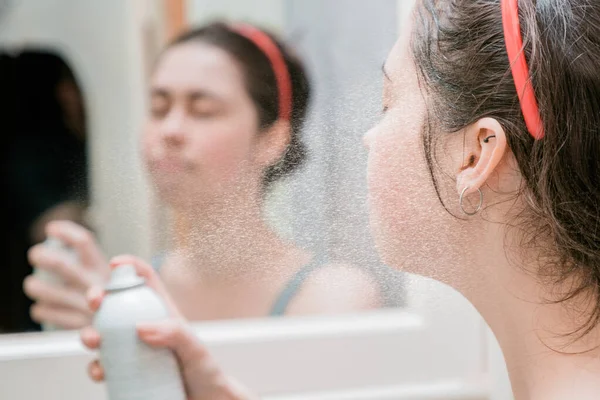 the girl uses a thermal spray from the bottle to refresh and moisturize the skin.