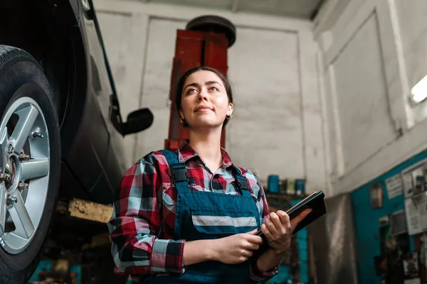 Portret Młodej Uśmiechniętej Białej Mechaniczki Mundurze Tabliczką Rękach Koło Samochodu — Zdjęcie stockowe