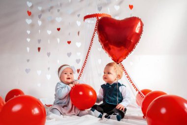 Kırmızı balonlarla poz veren süslü elbiseli iki şirin bebek. Sevgililer günü ve romantizm kavramı.