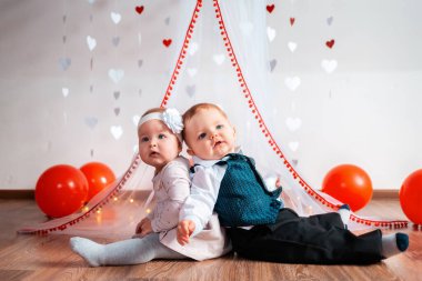 Kalpler ve balonlarla süslenmiş beyaz arka planda iki komik bebek poz veriyor. Sevgililer Günü konsepti.