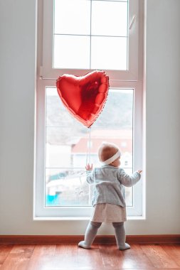 Sevgililer Günü. Küçük bebek pencereden dışarı bakıyor, kalp şeklinde kırmızı bir topla..