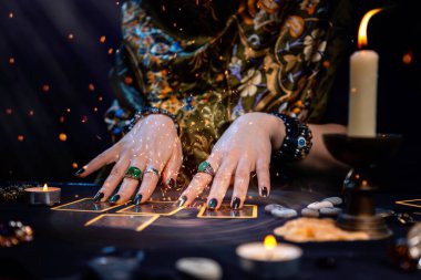 Haritacılık. Bir falcı Tarot kartları okur. Masanın üzerinde mumlar, fal baktıran nesneler ve kıvılcımlar var. Eller yukarı. Kehanet, astroloji ve ezoterizm kavramı..