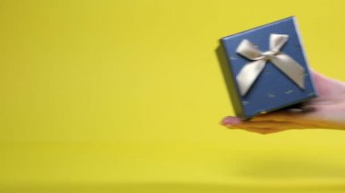 Bir kadının eli bir hediye tutar, kapağını açar ve fetüsün kesilmiş siluetini gösterir. Sarı arka plan. Hamilelik konsepti bir sürpriz..