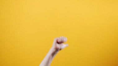 Bir kadının eli aşağıdan belirir ve baş parmağını kaldırır ve seğirir. Sarı arka plan. Pozitif iletişim ve jestler kavramı.
