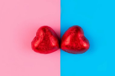 Sevgililer Günü ve LGBT ilişkileri kavramı. Kırmızı bir ambalajda iki kalp şeklinde çikolata. Arka plan pembe ve maviye bölünmüş. Boşluğu kopyala.