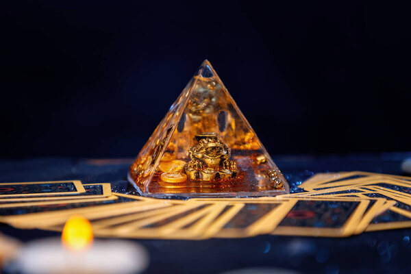 Стеклянная пирамида с золотой лягушкой. Карты Таро разбросаны по столу. Крупный план. Принято. Понятие гадания, магии и эзотерики.