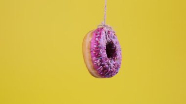 Bir ipin üzerinde asılı duran pembe şekerli bir donut, yavaşça ekseni etrafında döner. Sarı arka plan. Yumuşak odaklanma. Yakın plan..