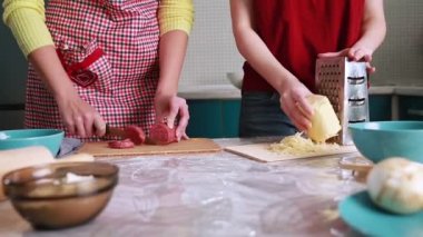 Ev yemeği. İki kadın yemek dilimliyor, sosis dilimliyor ve peynir ovuyor. Eller ve masa yakın plan..