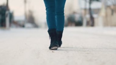 Karla kaplı bir yolda yürüyen bir kadın. Alt ve arka manzara. Bacakları yakın çekim. Yavaş çekim.