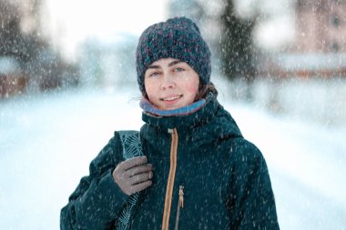 Şapka ve ceket giymiş gülümseyen beyaz bir kadının portresi. Kış mevsimi, kar yağışı.