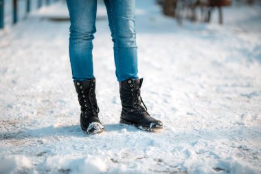 Kadın ayakları yakın planda, kayma önleyicili botlar giyiyor. Arka planda kar var. Boşluğu kopyala.