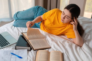 Yatağında uzanmış kitap okuyan genç bir kadının portresi. Çevrimiçi kurslar ve uzaktan eğitim kavramı. Üst görünüm.
