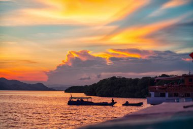 Suda yüzen bir tekne manzarası. Kıyı şeridinin arka planında ve güzel günbatımında.