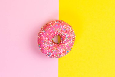 Pembe kremalı yuvarlak çörek. Pembe ve sarı arka plan. Uzayı kopyala Düz yatıyordu.
