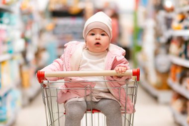 Alışverişe. Şirin bir çocuğun portresi bir süpermarketin ortasında bir alışveriş arabasında oturuyor. Aile alışverişi ve tüketim kavramı.