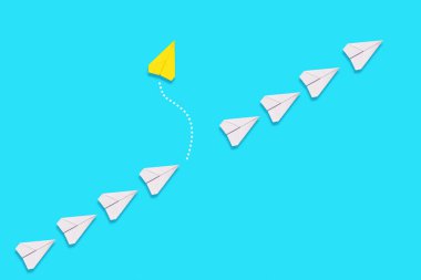 Bağımsızlık ve bireysellik kavramı. Sarı kağıttan bir uçak beyaz uçakların kuyruğundan uçar. Mavi arka plan. Düz yatıyordu.