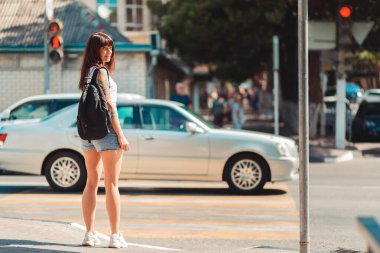 Bir kadın yaya geçidinin yanında duruyor. Arka planda, bir araba yol boyunca gidiyor ve trafik ışığı kırmızı. Trafik kuralları ve güvenlik kavramı.
