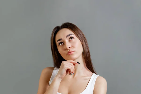 Concept of idea and information search. Portrait of a pensive young Caucasian woman looking up. Gray background. Copy space.