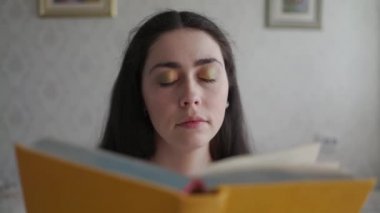 Genç bir kadın kitap okur ve gözlerini yorgunluk ve huzursuzlukla ovuşturur. Yakın plan..