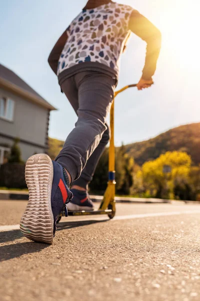 A teenage boy rides a scooter. Right foot in a sneaker close-up. Bottom and rear view. Empty street in Sunny weather in the background. Copy space. Concept of youth activity, sports and recreation.