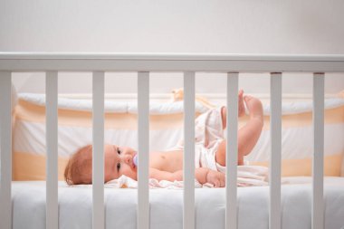 Beşikte uyuyacak bir bebek. Yakın plan. Beşiğin parmaklıklarından yan görünüş. Boşluğu kopyala.