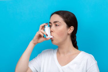 Astım spreyi kullanan genç bir kadının portresi. Mavi arka plan. Boşluğu kopyala.