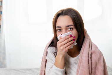 Genç, beyaz bir kadın, battaniyeyle örtülmüş, yüzünü mendille örtüyor. Evde tedavi görüyor. Uzayı kopyala Viral enfeksiyon ve karantina kavramı.