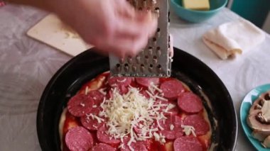 Ev yemeği. Bir kadın pizzanın üstünde peynir rendeliyor. Eller yukarı. Üst görünüm