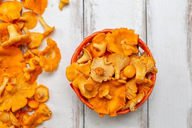 Hasır sepetin içinde turuncu mantarlar ve beyaz ahşap bir masanın sol tarafına yayılıyor. Kapatın. Dikey çizgiler.