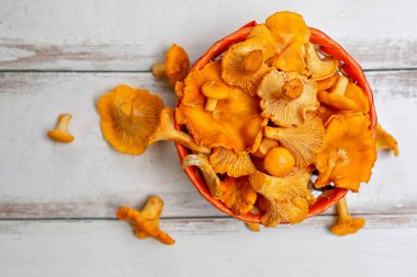 Hasır sepetin içinde portakallı mantarlar ve beyaz ahşap bir masaya saçılmış. Kapatın. Yatay çizgiler.