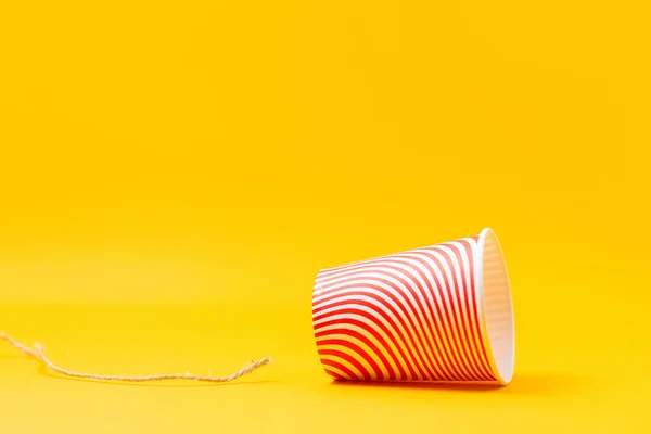 A red paper cup with a broken string. Children's homemade toy-walkie-talkie. Yellow background. Copy space. The concept of interrupting and disconnecting communication.