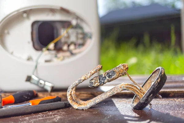 Aşınma ve pas yüzünden hasar gören su ısıtıcısı, ahşap bir masanın arka planında aletlerle yatıyor. Kapatın..
